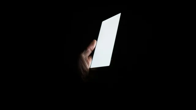 Hand hält ein leuchtendes Smartphone im Dunkeln – Grindr vs. Romeo im Vergleich