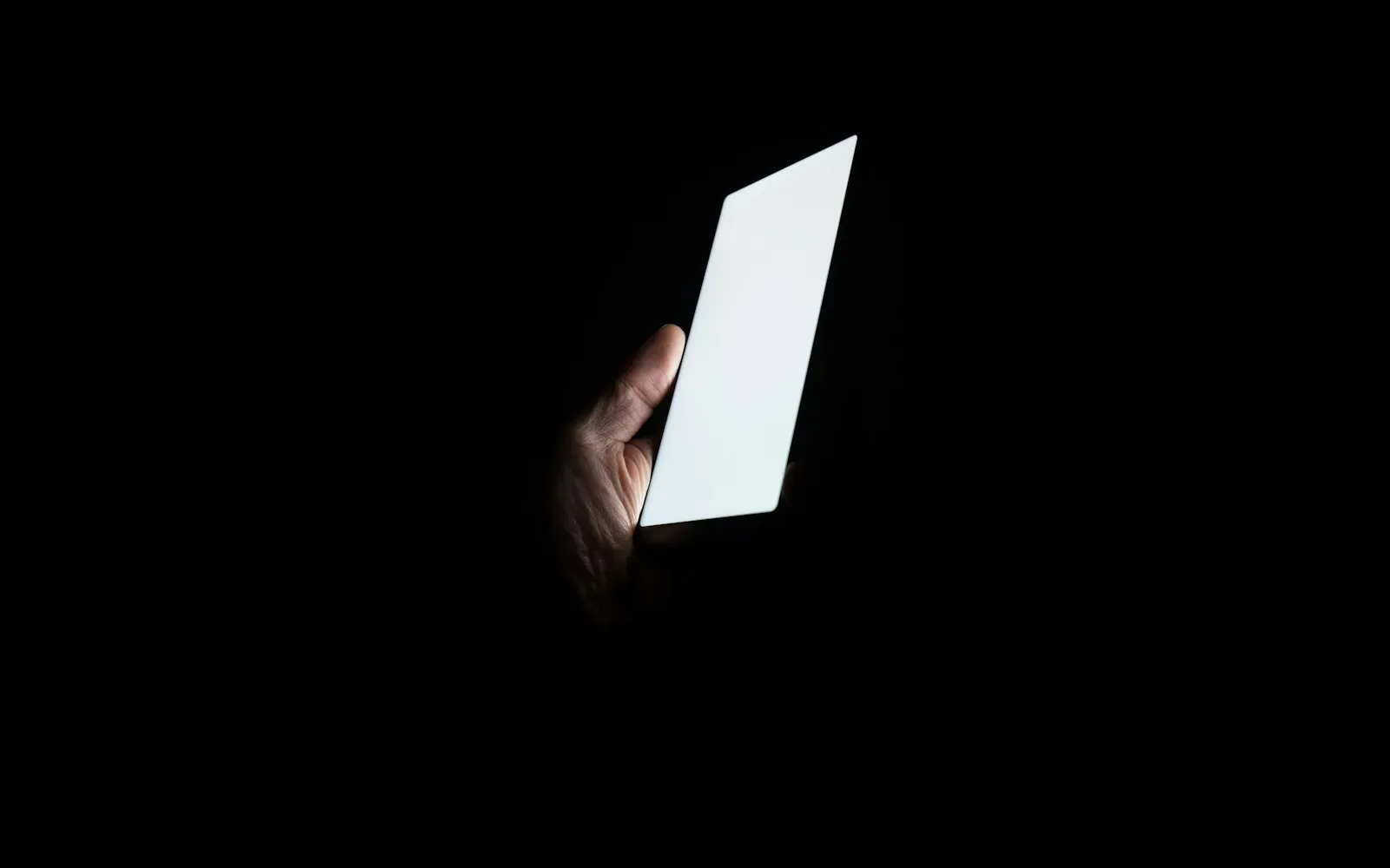 Hand hält ein leuchtendes Smartphone im Dunkeln – Grindr vs. Romeo im Vergleich