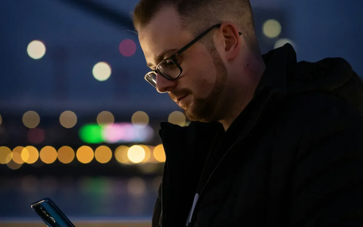 Mann schaut nachts in der Stadt auf sein Smartphone