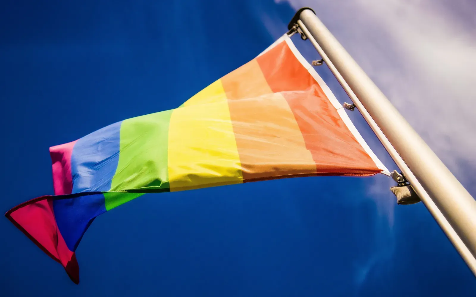 Regenbogenfahne weht an einem Fahnenmast vor tiefblauem Himmel – Bin ich schwul oder bi?