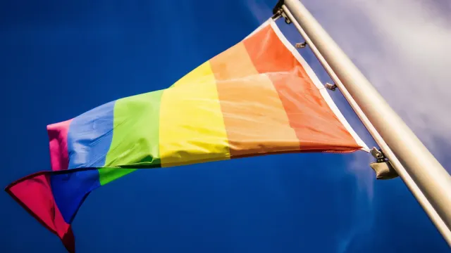 Regenbogenfahne weht an einem Fahnenmast vor tiefblauem Himmel – Bin ich schwul oder bi?
