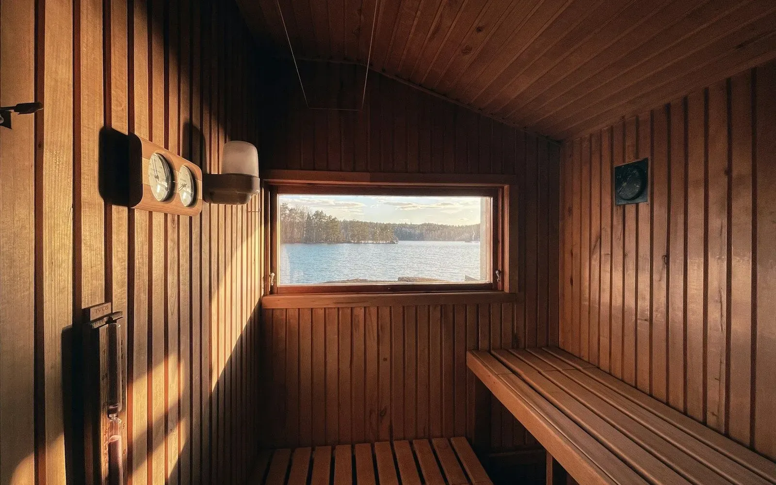 Leere Holzsauna mit Bänken und kleinem Fenster mit Blick auf einen See